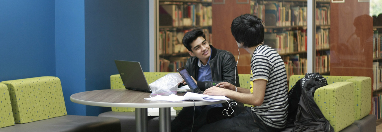 two students with laptops conversing in a SFU Library study space