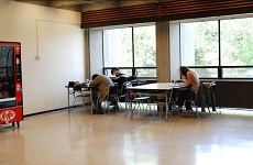 Students hunched over old tables in fairly empty space by windows.