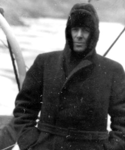 Black and white photograph of Harrison Brown wearing a wool coat and fur cap with ear coverings