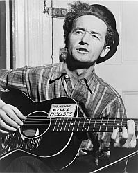 Woody Guthrie with his guitar, including the sticker, "This machine kills fascists."