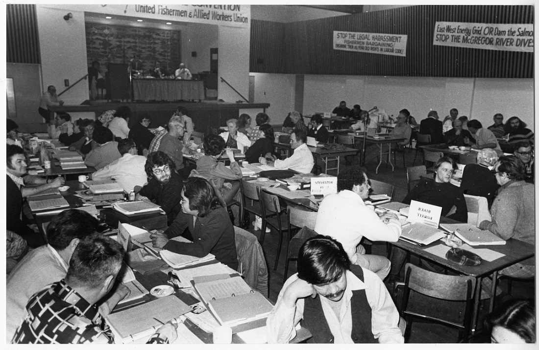 UFAWU members sitting at tables in a hall attending the 33rd annual convention. The tables are covered in notebooks and binders