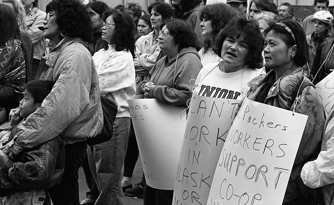 Group of protestors stand in with several protest signs