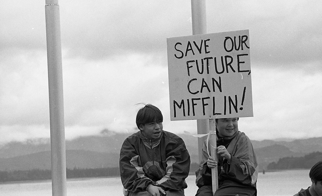 Two protestors sitting. One holds a sign that states: "Save our future, Can Mifflin!"