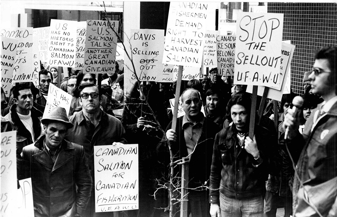 Large group of protestors outside of an office building, holding many signs