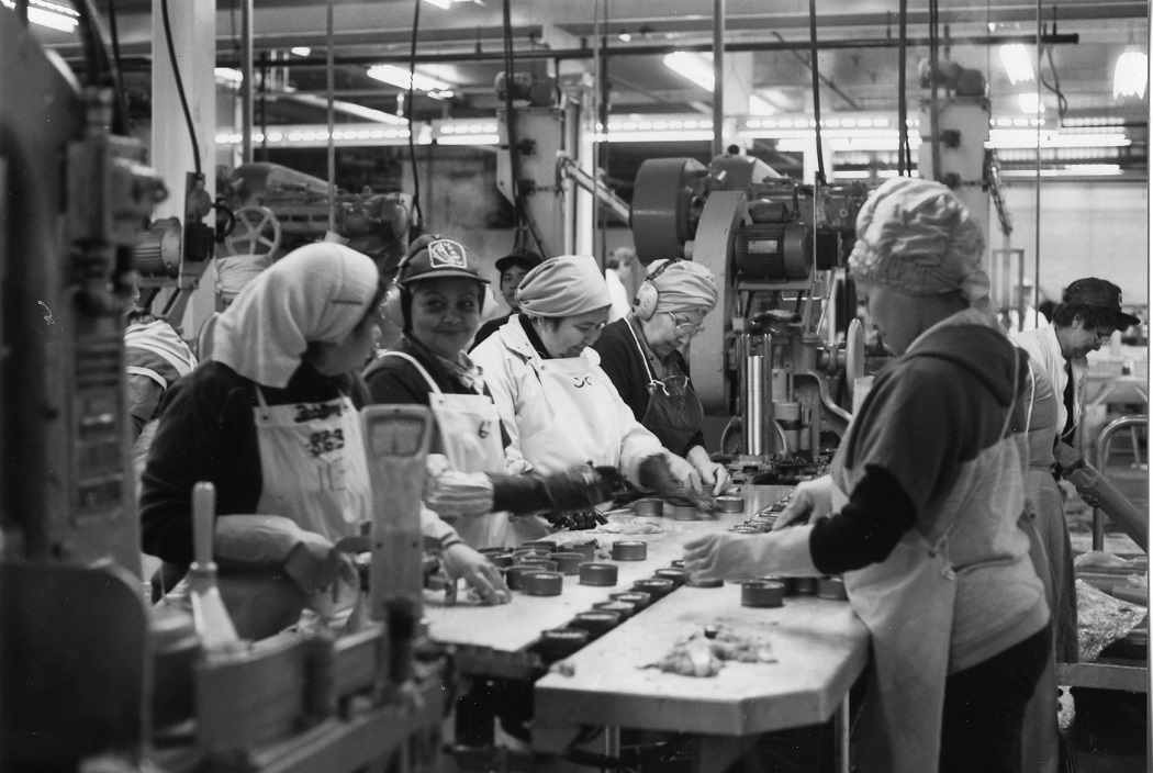 Five workers packing fish into cans inside the BC Packers cannery