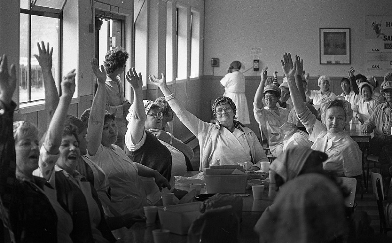 Women sitting at tables in the early 1980s raise their hands during a vote