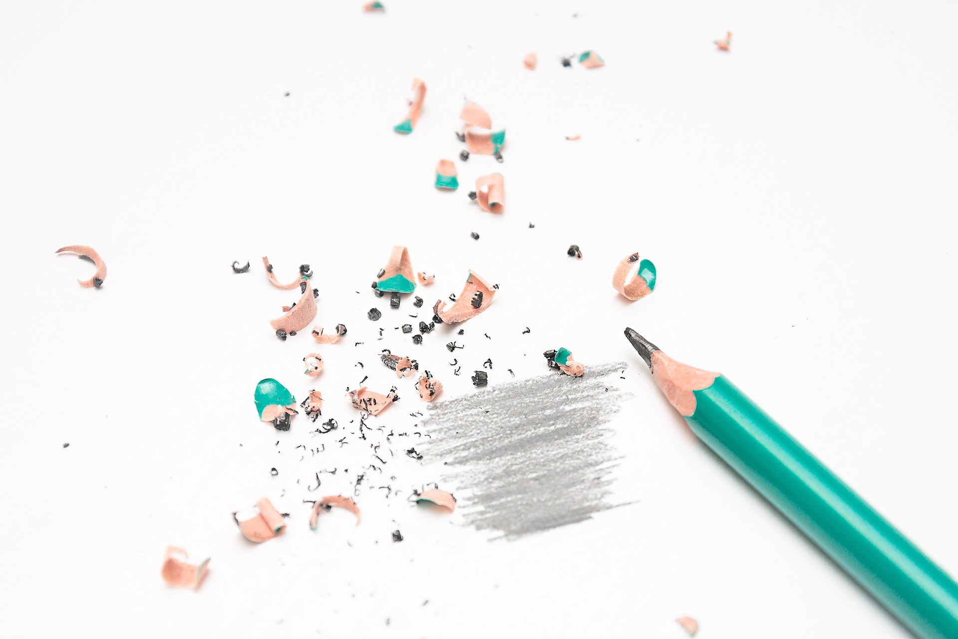 teal pencil surrounded by pencil shavings. Some grey shading on white paper.