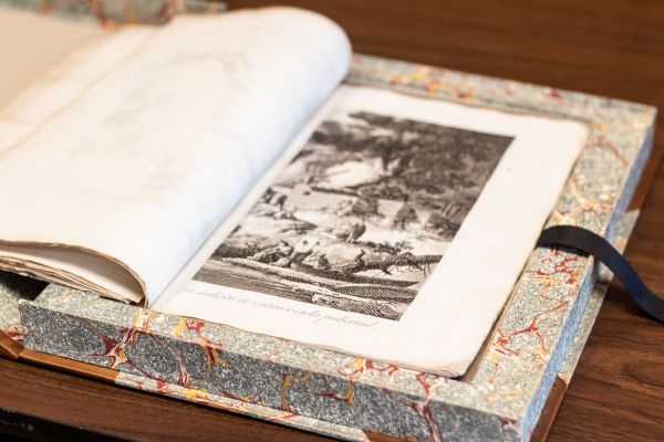 First edition atlas of a Spanish voyage to Nootka Sound and the Northwest Coast, inside a marble clamshell box, open to an engraved illustration of people by a body of water 