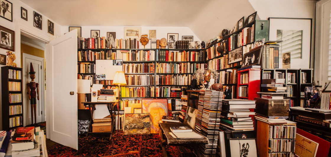 Photograph of the entrance to Robin Blaser's library, filled with many books, sculptures, and objects. This photograph was taken by photographer Christos Dikeakos