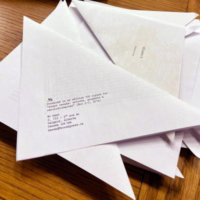 Detail of the chapbook collection Avant Canada (2014) featuring poems by many different Canadian poets. Each poem is printed on a sheet of paper folded into an iscosoles triangle. 