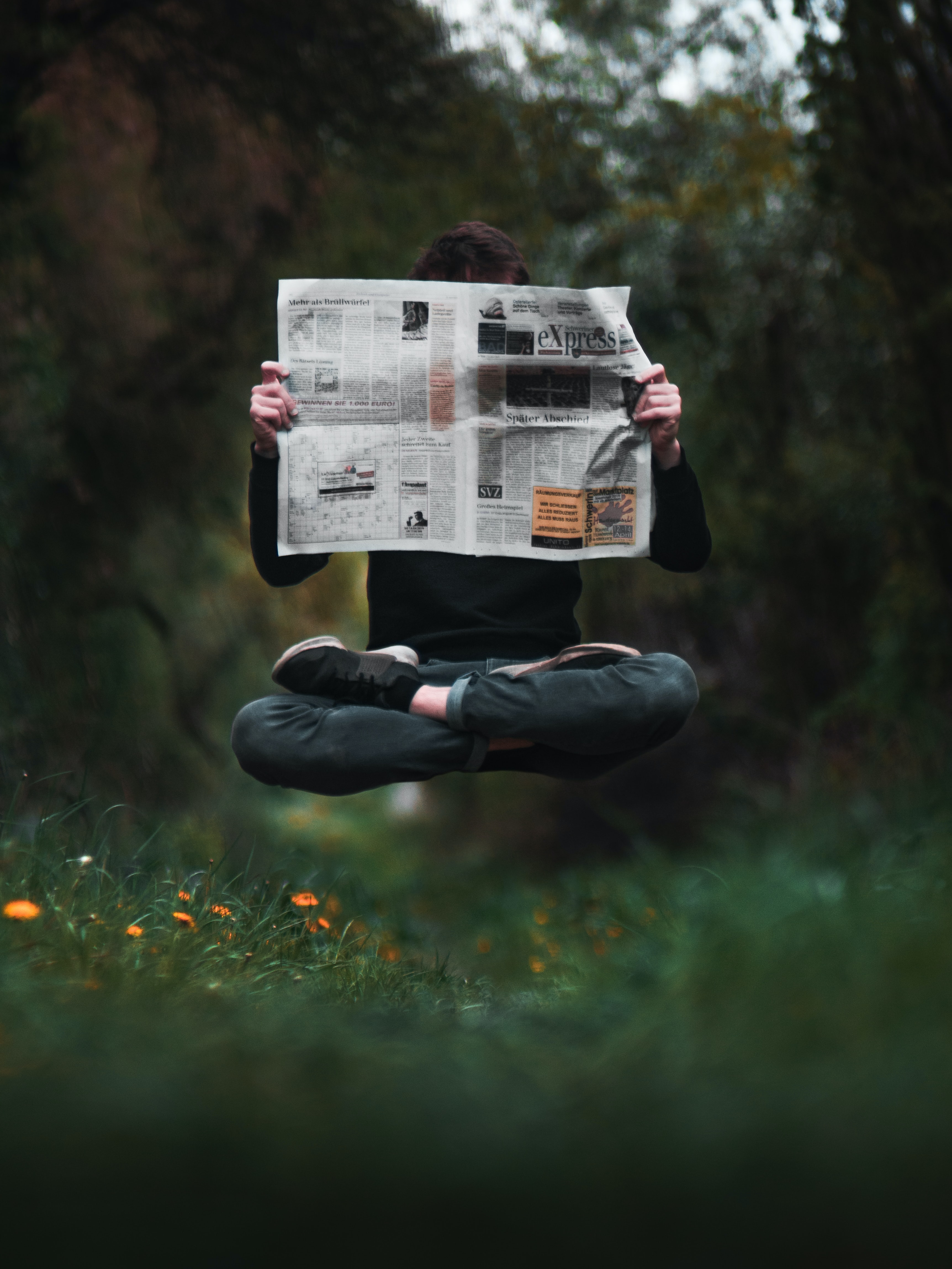 Photo of a cross-legged person reading a newspaper while levitating