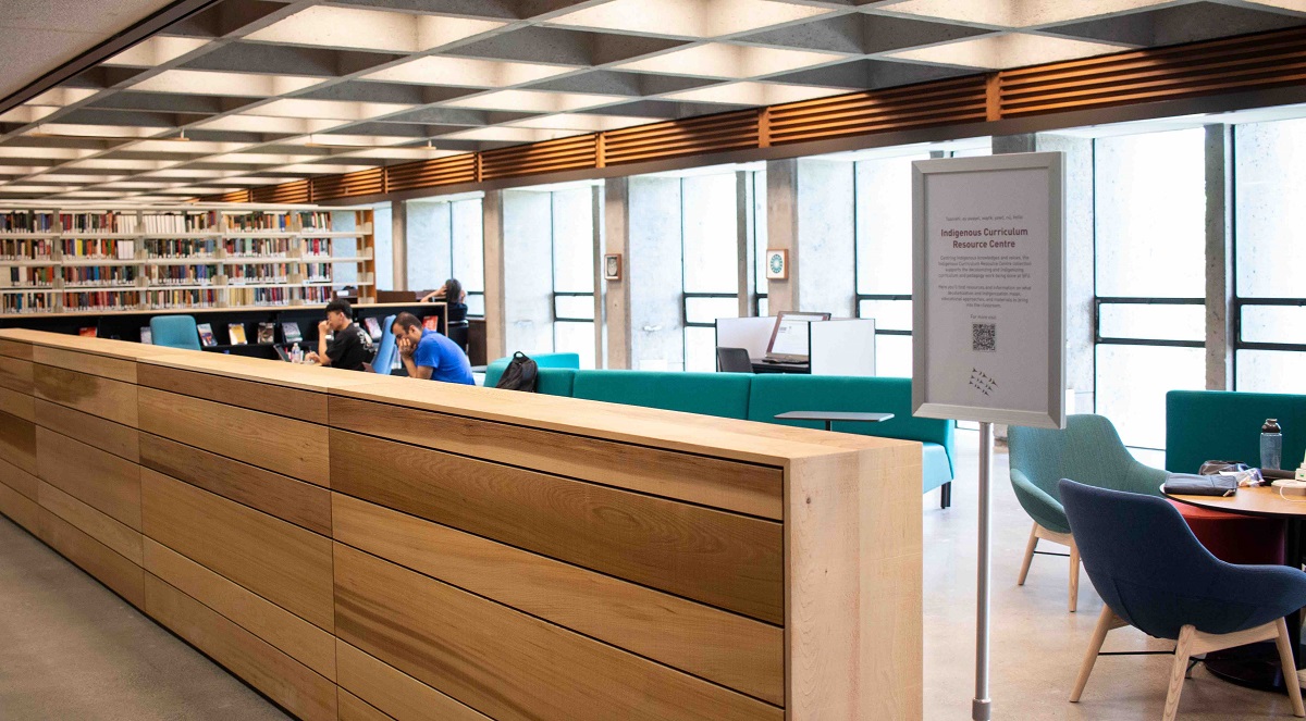 Image with the cedar plank bookcases in the foreground, and a glimpse of the couches and windows in the background.