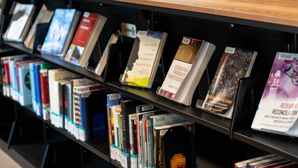 Image of a bookcase, with two shelves. One shelf has books displayed with the covers facing out, the other has the books with their spines out.