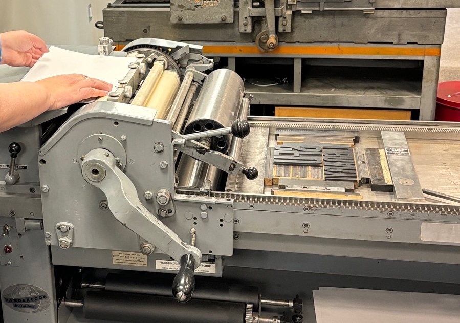 Hands putting paper into the rollers of a printing press.