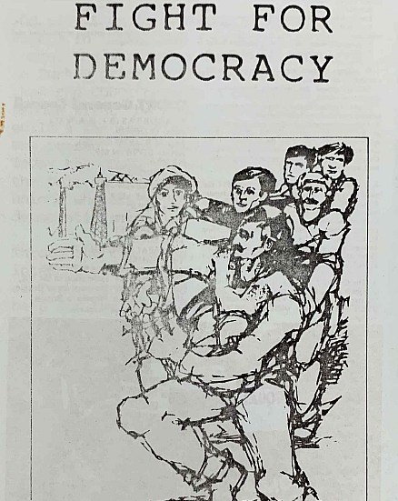 Detail of a pamphlet for the Committee for Defence of Democratic Rights in Turkey, featring a man holding a child, directing other Turkish workers with his hand